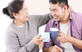 A mother and son holding coffee cups and smiling at each other