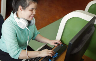 Asian young blind woman with headphone using computer with refreshable braille display or braille terminal a technology device for persons with visual disabilities